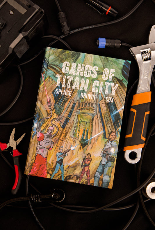 Book titled 'Gangs of Titan City' by Spence, Brown & Cox on a black surface with tools.